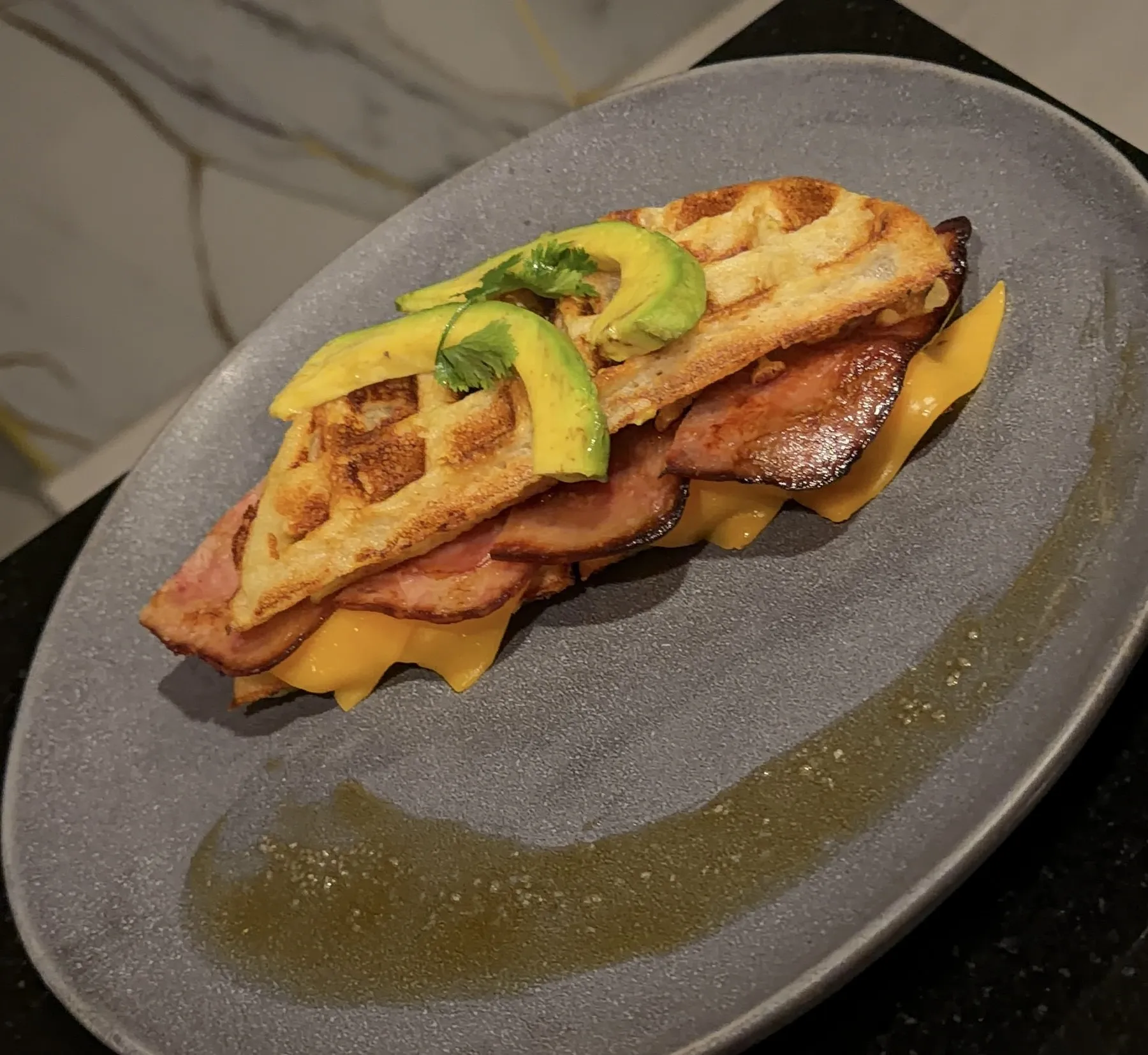 Sándwich waffle de buñuelo con queso cheddar, tocineta y aguacate